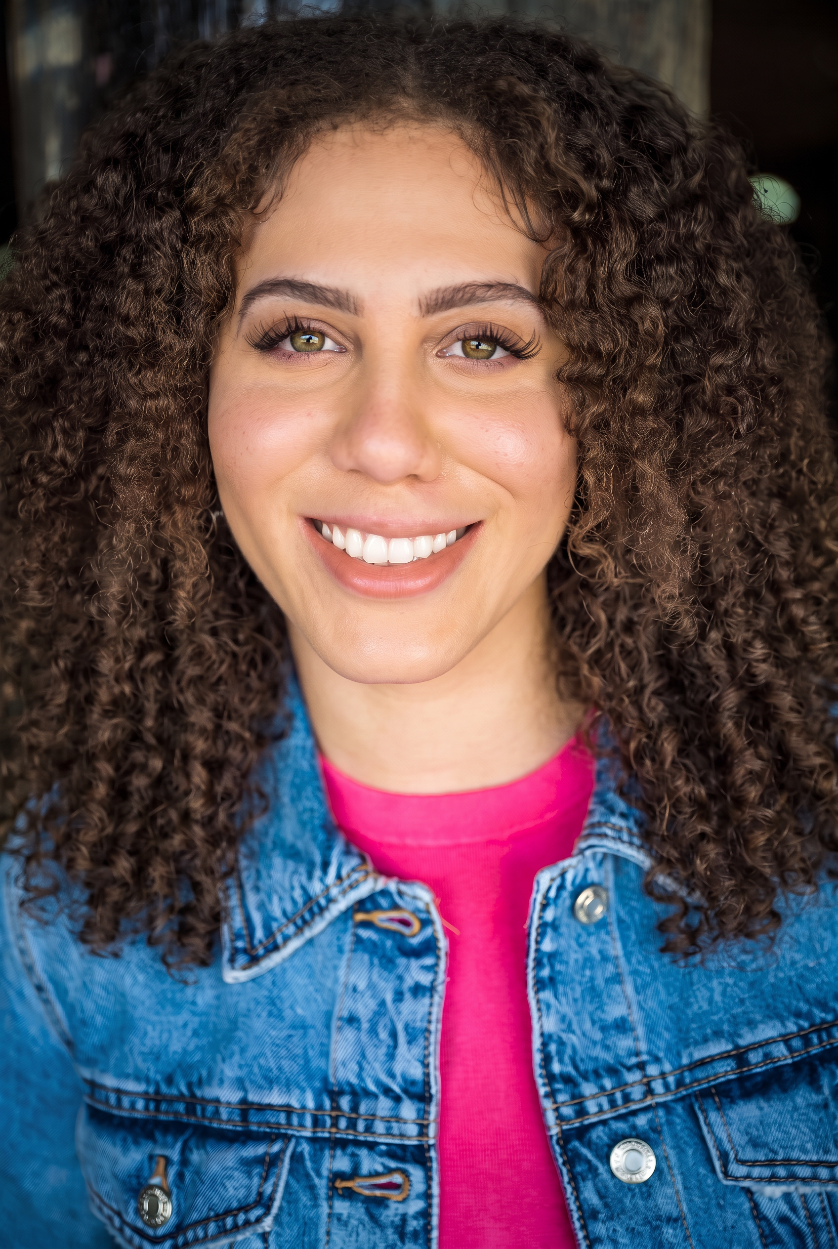 Smiling close headshot of Ashlyn in a denim jacket over a pink top.
