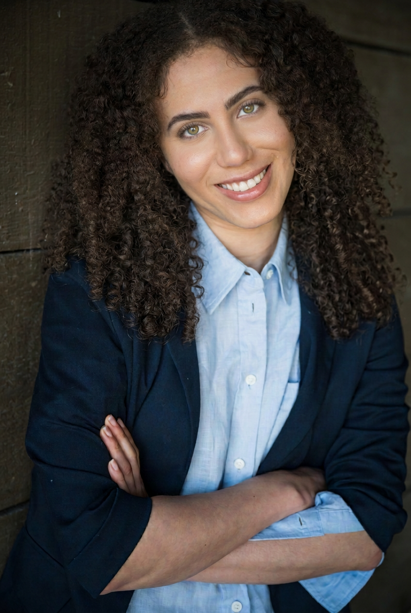 Ashlyn Nichols in a navy blazer, natural curls and a direct, warm expression.